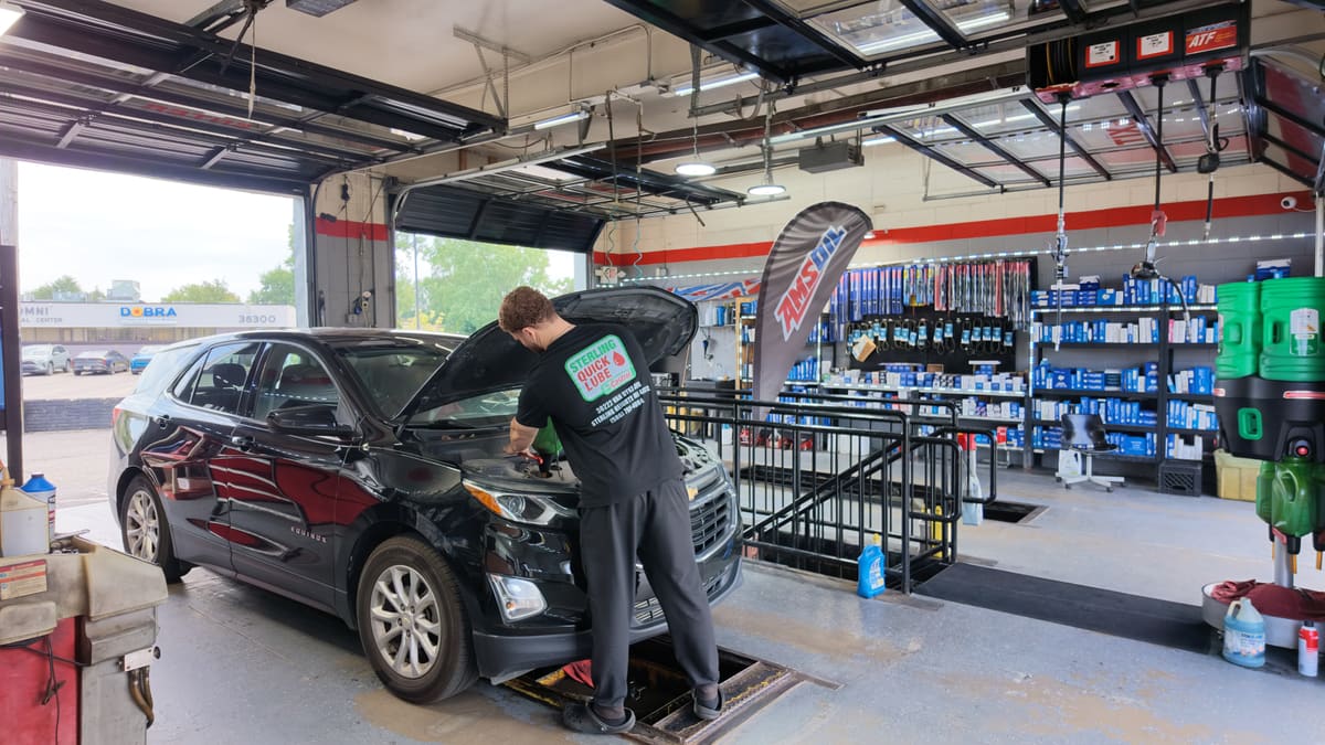 Sterling Quick Lube technician working under the hood of a black Chevrolet Equinox during a full-service oil change